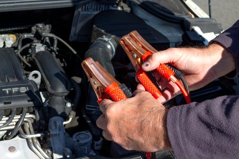 Mains qui tiennent des pinces de survoltage rouge et noire au-dessus d'un moteur